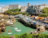 En vacker vy över hamnen i Biarritz med båtar i vattnet och en kyrka i bakgrunden. Kanske är det här tåg till Biarritz tar dig.