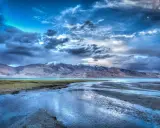 Paesaggio montano con lago e fiume, cielo drammatico con nuvole scure e luna, effetto HDR.