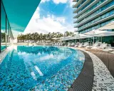 Luksusowy basen z mozaiką i leżakami, otoczony sosnami, przy nowoczesnym hotelu. Idealne miejsce na relaks, jak na plaży w Międzyzdrojach.