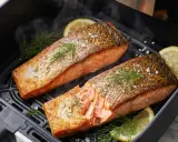 Zwei saftige Lachsfilets mit knuspriger Haut, garniert mit Dill und Zitrone, dampfen im Airfryer.