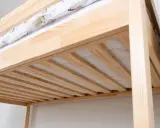 Drewniana antresola w domu, z widocznym materacem i pościelą w delikatny wzór. Solidna konstrukcja z sosnowego drewna.