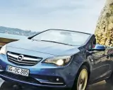 Niebieski Opel Cascada z opuszczonym dachem jedzie po mokrej drodze przy skalistym wybrzeżu.