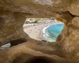 Blick durch Höhle auf Strand von Matala, Kreta. Ein sonniges Hippie-Dorf mit bunten Häusern und blauem Meer.