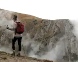 Person med ryggsäck och stavar, övar stavgång teknik på en bergssluttning med dimma.