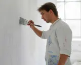 Un peintre applique un enduit rebouchage chaux sur un mur, préparant la surface pour une fresque.