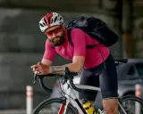 Mężczyzna w różowej koszulce i czarnych spodenkach rowerowych, kasku i okularach. Idealny strój, gdy zastanawiasz się, jak się ubrać na rower 15 stopni.