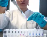 Naukowczyni w niebieskich rękawiczkach precyzyjnie pipetuje fioletowy płyn do probówki. To kluczowy etap w badaniach nad leczeniem biologicznym.