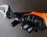 Mano enguantada sujeta llave inglesa ajustable, herramienta esencial para saber para que sirve la llave inglesa al apretar o aflojar tuercas y tornillos.