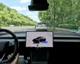Interno di una Tesla in movimento in Europa, con il sistema FSD attivo. La strada è fiancheggiata da alberi verdi.