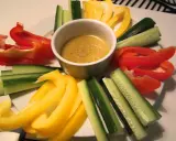 En skål med bagna cauda-sås omgiven av färgglada grönsaksstavar: röd och gul paprika samt gurka.