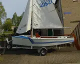 Un petit voilier blanc et bleu, un vaurien bateau prêt pour l'aventure, est sur sa remorque.