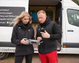 Ein Mann und eine Frau halten eine Drohnenfernbedienung. Auf dem Van stehen "Drohnenschulungen" und "Kitzrettung". Informiere dich über die drohnenführerschein kosten.