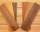 Verschiedene Holzproben mit unterschiedlichen Farben und Maserungen liegen auf einer Holzoberfläche. Sie zeigen die Vielfalt der dauerhaftigkeitsklassen holz für Terrassendielen.