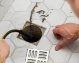 Ein Mann reinigt einen Duschabfluss mit einer Spirale. Der Abfluss stinkt, ist aber nicht verstopft. Haare und Schmutz werden entfernt.