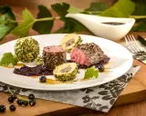 Edles Fleischgericht mit Johannisbeeren verwerten: zartes Rinderfilet, umhüllt von Kräutern und Nüssen, serviert mit einer fruchtigen Johannisbeersauce und Beilagen.