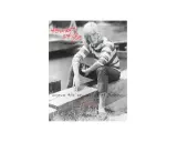 A woman with short blonde hair embodies tomboy style, wearing a striped shirt and jeans, sitting on a wooden beam. Text reads "tomboy style" and "beyond the boundaries of fashion.