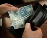 Ręce wkładają polskie banknoty 50 zł do czarnego portfela. To kieszonkowe dla dziecka na drobne wydatki.