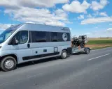 Srebrny kamper z motocyklem na przyczepie jedzie drogą. Przygoda w Szwecji kamperem dopiero się zaczyna.