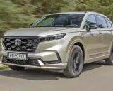 Nowy Honda CR-V w kolorze złotym jedzie po drodze, otoczony zielenią.