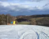 Śnieżny stok narciarski z armatkami śnieżnymi i widokiem na pagórkowaty krajobraz.