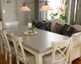 Ett grått bord med vita stolar och en vit bänk med kuddar. Planerar att måla ekbord svart för en modern look.