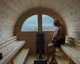 Man njuter av värmen i en bastuflotte i Skåne med utsikt över havet och en fyr.