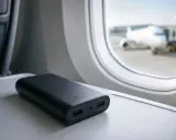 Czarny powerbank na stoliku w samolocie, z widokiem na samolot przez okno.