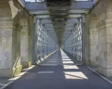 El **puente internacional Tui** se alza imponente, un túnel de metal y piedra que se pierde en la distancia, proyectando sombras geométricas sobre el asfalto.