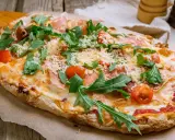 Eine leckere Pinsa belegen mit Schinken, Rucola und Kirschtomaten. Käse und Tomatensauce runden den Genuss ab.