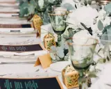 Eleganckie nakrycia stołu na wesele bez alkoholu: zielone kieliszki, menu, ozdobne pudełeczka i bukiety.