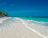 En vit sandstrand med turkost vatten och palmer vid Kendwa, Zanzibar. Båtar guppar i fjärran.