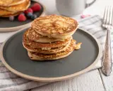 Stos puszystych fit pancakes z odżywki białkowej, ozdobiony malinami i borówkami, czeka na widelcu.