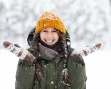 Una chica sonríe felizmente en medio de una nevada, con su gorro naranja y guantes a juego. ¡Bonitas fotos en la nieve!