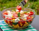 Szybkie i tanie sałatki to idealny pomysł na lekki posiłek. W szklanej misce kolorowa sałatka z pomidorów, ogórka, kukurydzy, papryki, sera feta i tuńczyka.
