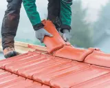 Dachówka ceramiczna w rękach dekarza. Czy remont dachu wymaga pozwolenia na budowę? Zależy od zakresu prac.