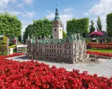 Miniatura ratusza z wieżą zegarową, otoczona czerwonymi kwiatami. Jedna z wielu atrakcji Kotliny Kłodzkiej.