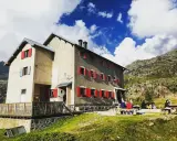 Rifugi raggiungibili in auto a Bergamo: un edificio con persiane rosse in montagna, con persone sedute fuori.