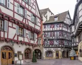 Fachwerkhäuser mit roten und weißen Fassaden in der Colmar Altstadt, geschmückt mit Lichterketten und Weihnachtsdekoration.
