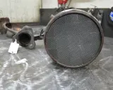 Zużyty filtr cząsteczek stałych, element układu wydechowego pojazdu, leży na metalowym blacie.