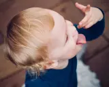 Małe dziecko nie słucha w przedszkolu, wyciąga język i bawi się jedzeniem.