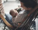 Ein Baby schläft friedlich auf dem Arm einer Person, die in einem Schaukelstuhl sitzt. Es ist, als ob die Babys im Bauch noch träumen, bevor sie die Welt entdecken.