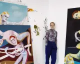 A woman stands in her studio surrounded by her surreal, figurative paintings, showcasing her as one of today's popular contemporary artists.