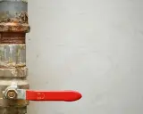 Tubería oxidada con una llave de paso general roja, lista para controlar el flujo.