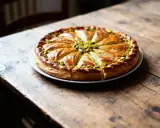 Une galette des rois à la pistache, dorée et appétissante, garnie de pistaches concassées, sur une table en bois rustique.