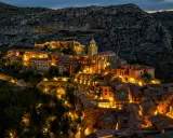 Pueblo iluminado al anochecer, ideal para planes para el puente de diciembre. Casas de piedra y tejados se asoman entre la montaña.