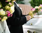 Białe i różowe róże, często wybierane jako kwiaty na pogrzebie starszej osoby, zdobią trumnę.