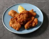 Chrupiący kurczak karaage na niebieskim talerzu, z kawałkiem cytryny.