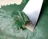 Espátula metálica retirando pintura verde descascarada de una pared. Proceso de cómo quitar pintura de la pared.