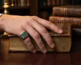 Mano con anello dal significato esoterico, con pietre verdi, appoggiata su un antico libro rilegato in pelle.