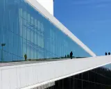 Nowoczesna architektura Uniwersytetu w Oslo z lustrzaną fasadą odbijającą niebo i ludzi.